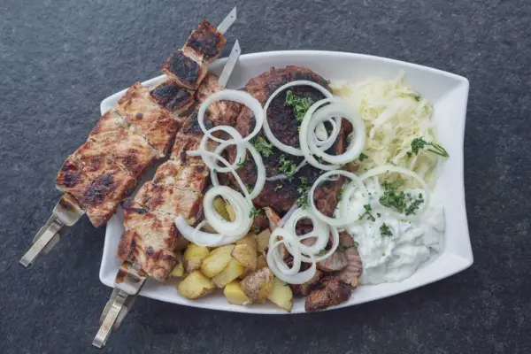 Ein Teller mit gegrilltem Fleisch, Kartoffeln und Krautsalat, garniert mit Zwiebelringen. Ein authentisches Souvlaki Rezept original.