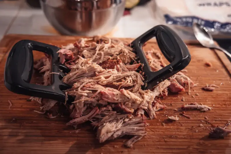 Pulled pork mit Fleischgabel auf Holzbrett. Perfekt für Smoker Rezepte Schwein, z.B. Pulled Pork Sandwiches.